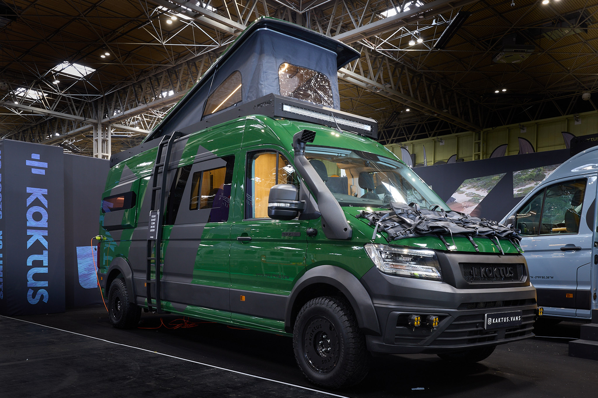The Kaktus Adventure Vans Oasis x4 has a dark green and dark grey exterior with prominent decals.  There is an external ladder leading to the pop top roof which is fully extended.