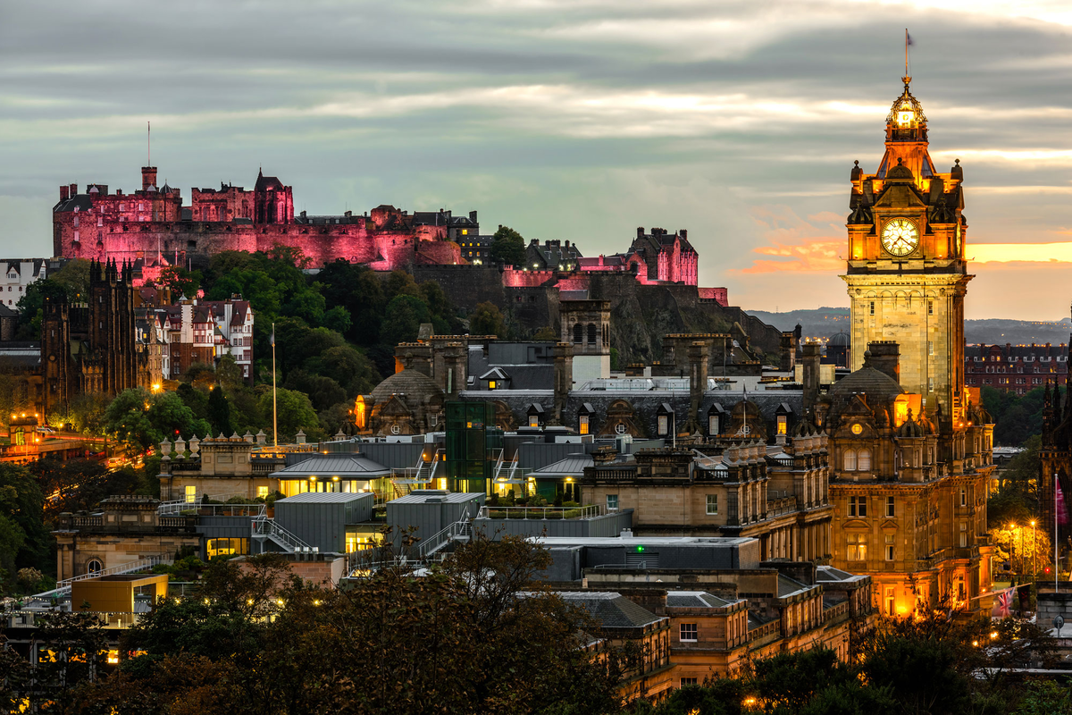 view of Edinburgh city centre and the castle lit up as the sun sets over the city