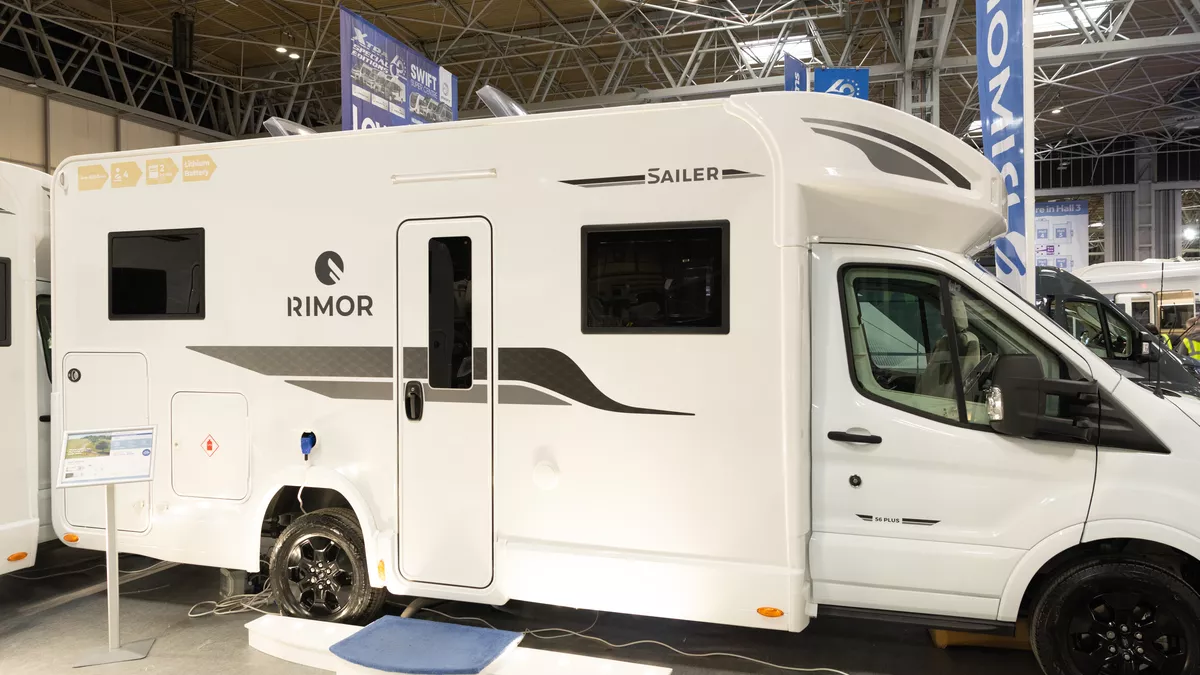 The Rimor Sailer Plus 56 has a white exterior, decorated with black and grey decals.  There is a large step outside the habitation door with a small stand to the left.