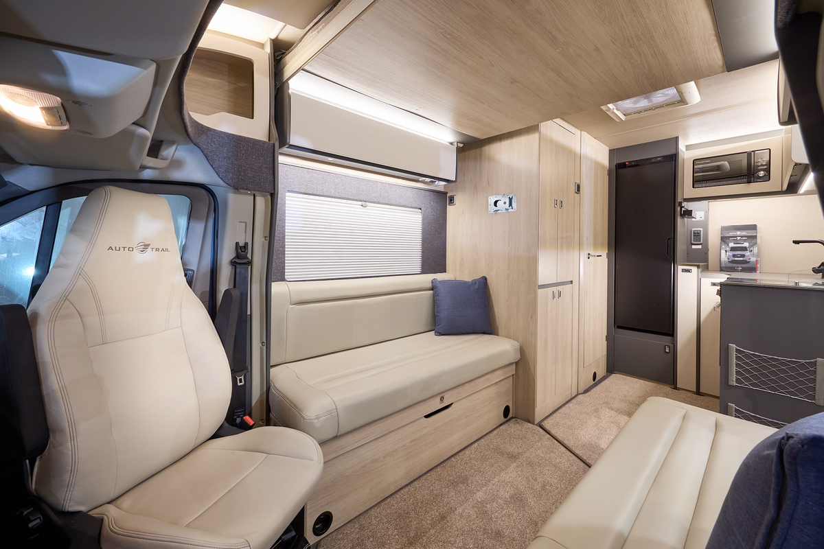 The Auto-Trail F-Line F62 has beige carpets, with pale wood cabinets with cream overhead lockers.  The upholstery is cream leather.  There is a rear kitchen with a black fridge freezer and microwave in an overhead cabinet.