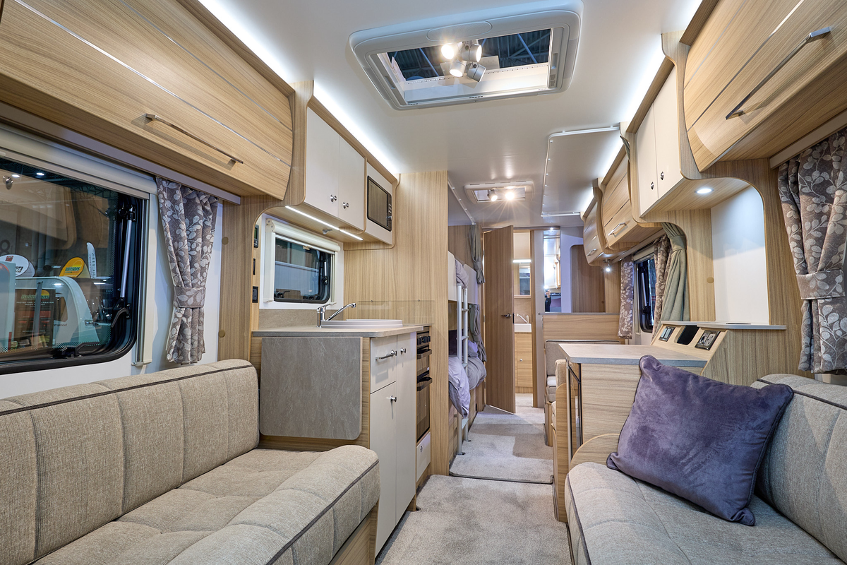Bailey Phoenix 762 interior, it is beige with light wood.  There are bunk beds with a fitted ladder beyond the kitchen.  The rear washroom has a wooden door which is open.  There are two skylights.