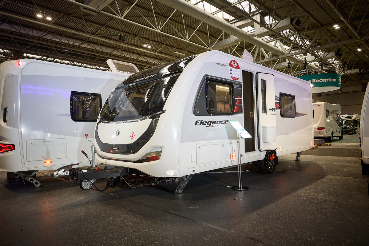 Swift Elegance Grande 780's exterior is white with a large front window.  There are black graphics on the front panel.  The door is open and its corner steadies are down.