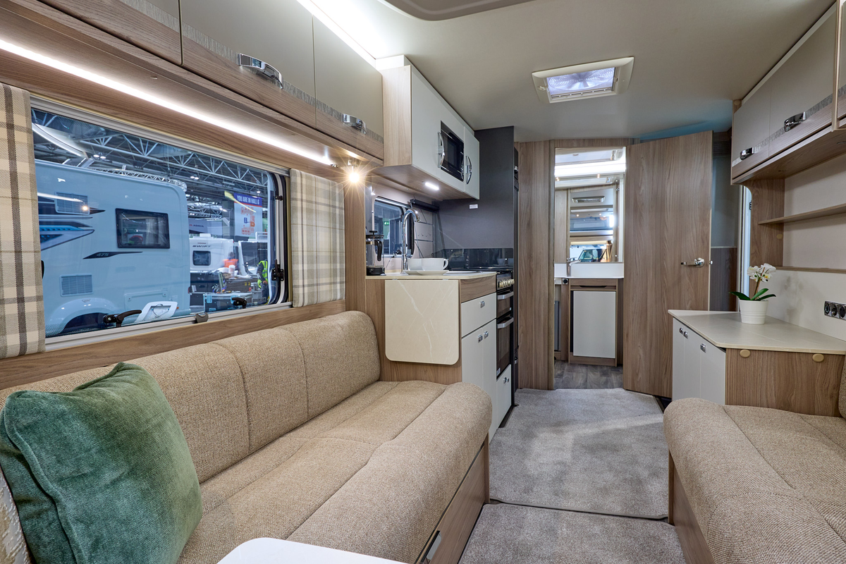 Swift Challenger SE 480's interior has pale wooden furniture with beige upholstery.  The washroom is at the rear and its door is open.