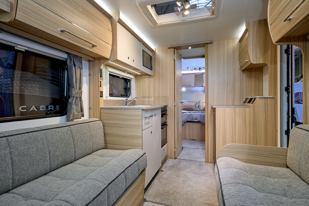 Bailey Phoenix 640 interior, it is grey with light wood.  There is a fixed bed beyond the kitchen and the bedroom has a wooden door.  There are two skylights.