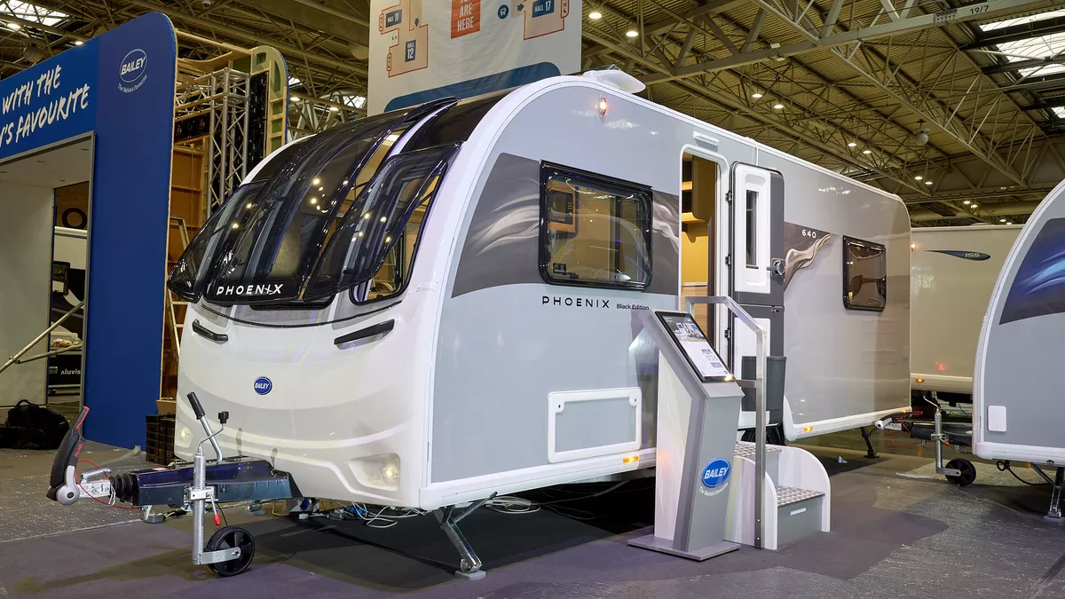 The Bailey Phoenix Black 640 has a grey exterior and a brown decal with light ripples on it.  The entrance door is open and there are two metal steps to gain easy access to the interior.  Next to the steps is an interactive stand.