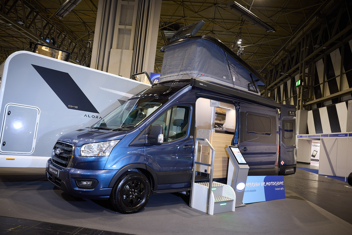 The Bailey Endeavour B65 is blue with black trim.  There is an interactive stand by the open sliding door which reveals the interior.  The pop top roof is fully open.