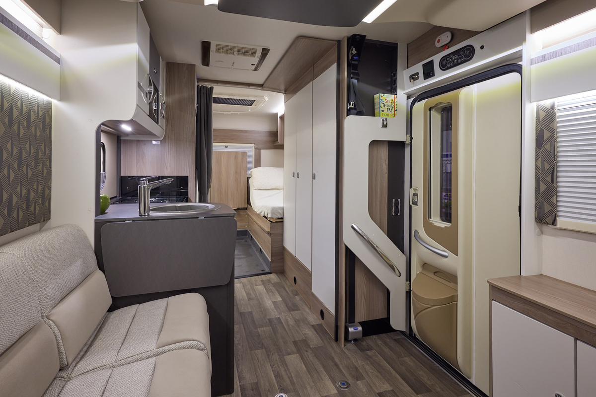 The Coachbuilt GB LIV Swift Escape 674 has a wooden floor, with cream cabinets.  The upholstery is cream and light brown.  There is fixed rear bed, close to the en suite washroom.