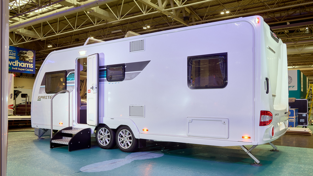 Swift Sprite Quattro Grande FB’s exterior is white.  There is a turquoise decal to the right of the side window with the Union flag.  The entrance door is open and there are two metal steps to gain easy access.  The two roof lights are open.
