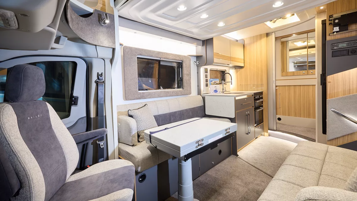 The Bailey Adamo 69-4 has beige carpets, with cream and pale wood cabinets.  The upholstery is cream and dark brown.  There is a step to the rear washroom.  There is a folded table in front of one of the sofas.