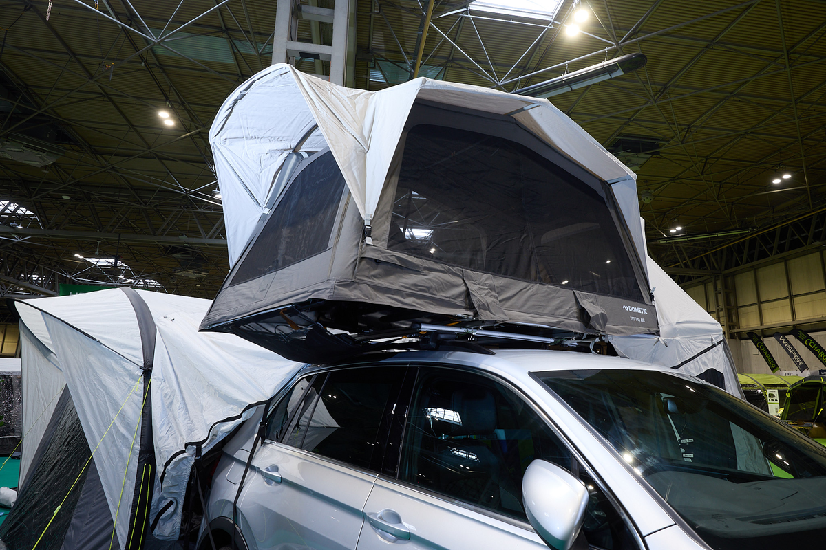 The Dometic TRT 140 AIR is displayed on a silver Volkswagen.  It has grey and white canvas and has an annex to the rear of the vehicle.  The tent is sitting on top of two roof bars.