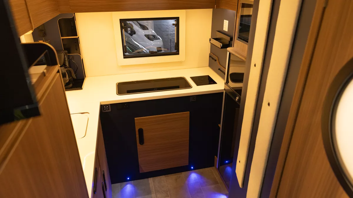 The Rimor Sailer Plus 56 has a rear kitchen.  The cabinets are wooden with brown accents.  There is a rear window behind the sink and hob.