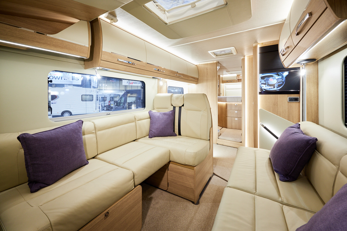 Auto-Trail Grande Frontier GF-88 has cream leather upholstery, with wooden furniture.  The floor has beige carpet.  The overhead lockers are cream with wooden surrounds.  There are four purple cushions