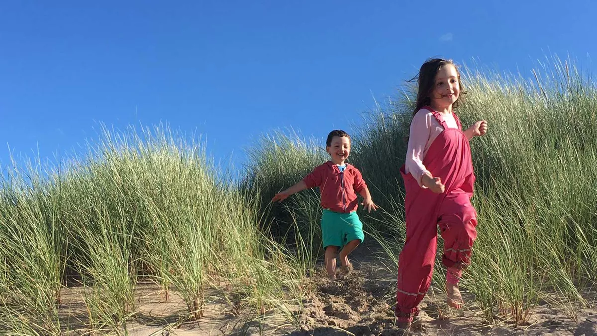 Happy children running down the dunes at Freshwater East