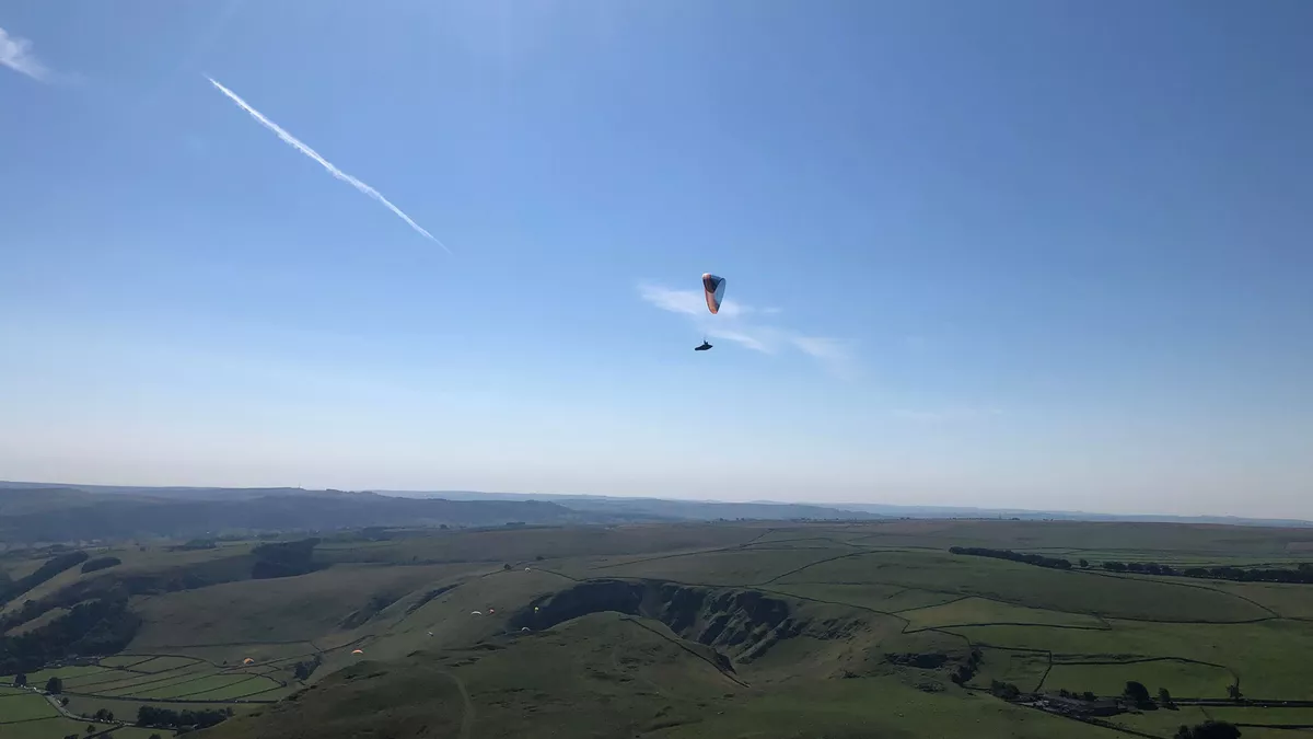 A solo paraglider floating in clear skies over the Peak District