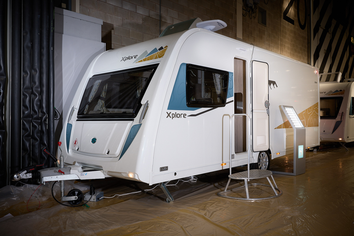 Xplore 554's exterior is white with turquoise and gold graphics, the door is open and there's a metal step for easy access into the interior.