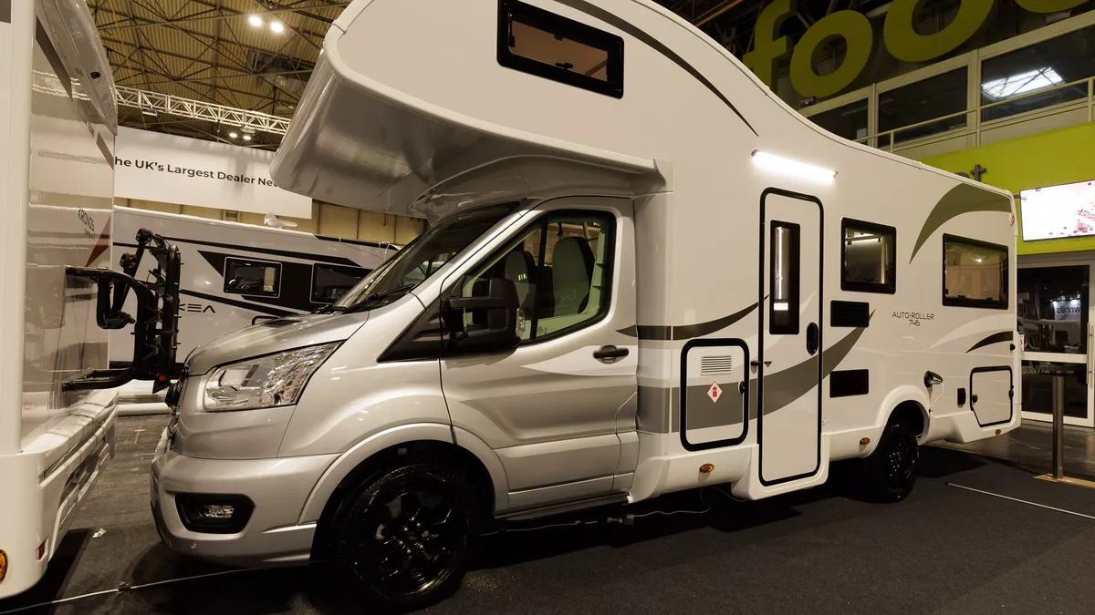 The Roller Team Auto-Roller 746 has a silver cab and white coachbuilt body.  It has black trims around the doors with bronze decals.  