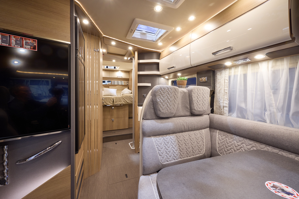 The Carthago C2-tourer I 148 RB-QB has a wooden floor, with cream cabinets.  The upholstery is grey  with white stitching.  There is a step up to the rear fixed bed.