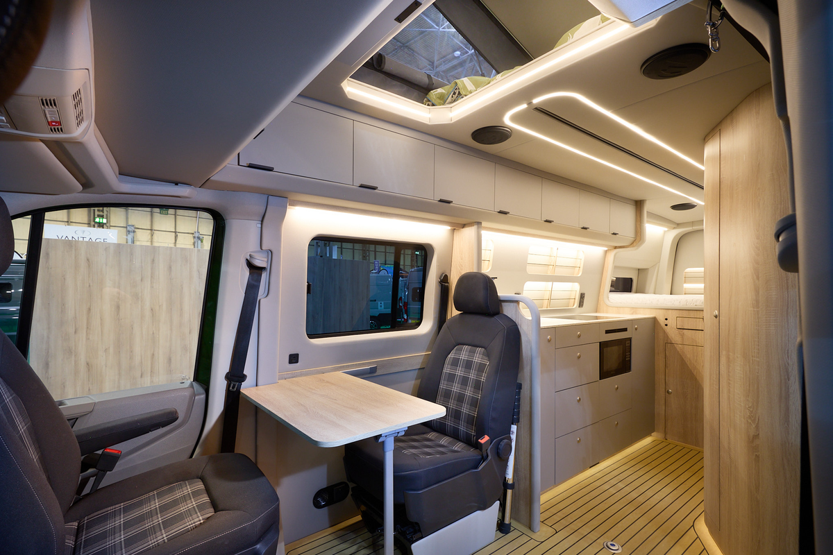 The Kaktus Adventure Vans Oasis x4 has a wooden floor.  The upholstery is two tone brown with a tartan pattern.  The cabinets are all pale wood.  The pop top roof is extended.