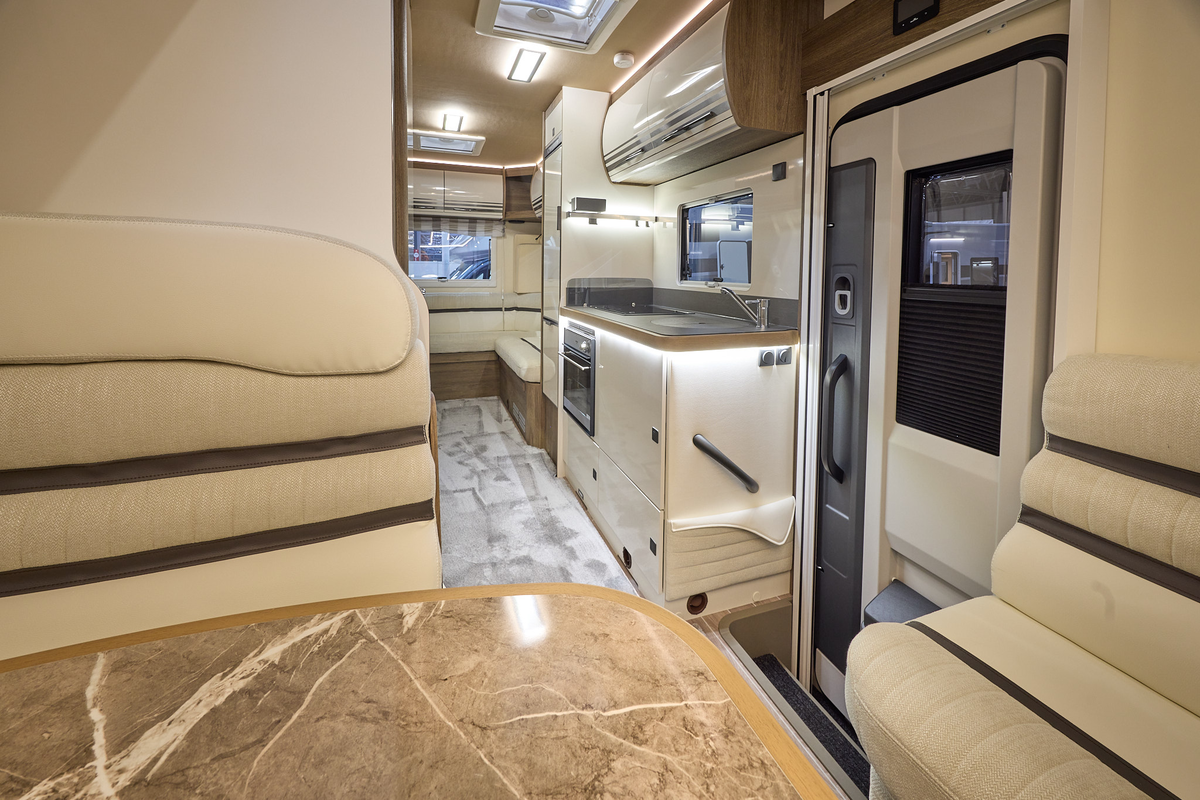 The Roller Team Pegaso 745 has grey carpet.  The upholstery is cream leather with dark brown highlights.  There is a marble effect table in front of the sofas.  The cabinets are cream with wooden surrounds.  There are two skylights.