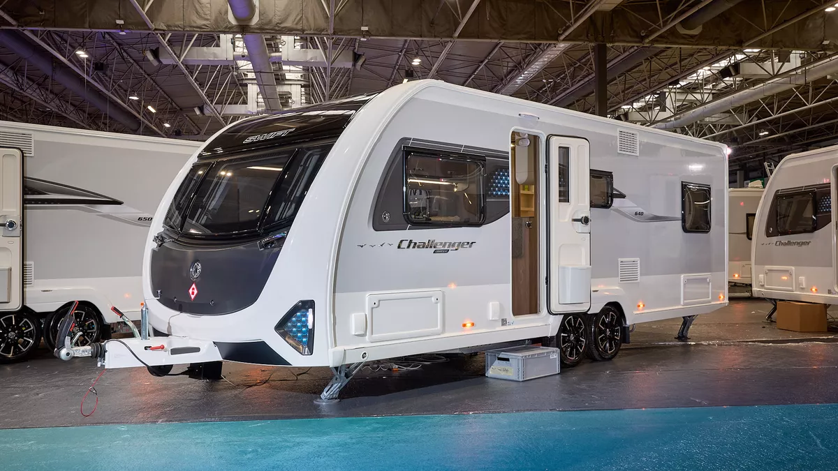 Swift Challenger Grande 640 is white with grey sides and a black front panel.  There are turquoise triangular panels at the front.  Its corner steadies are down and its entrance door is open.
