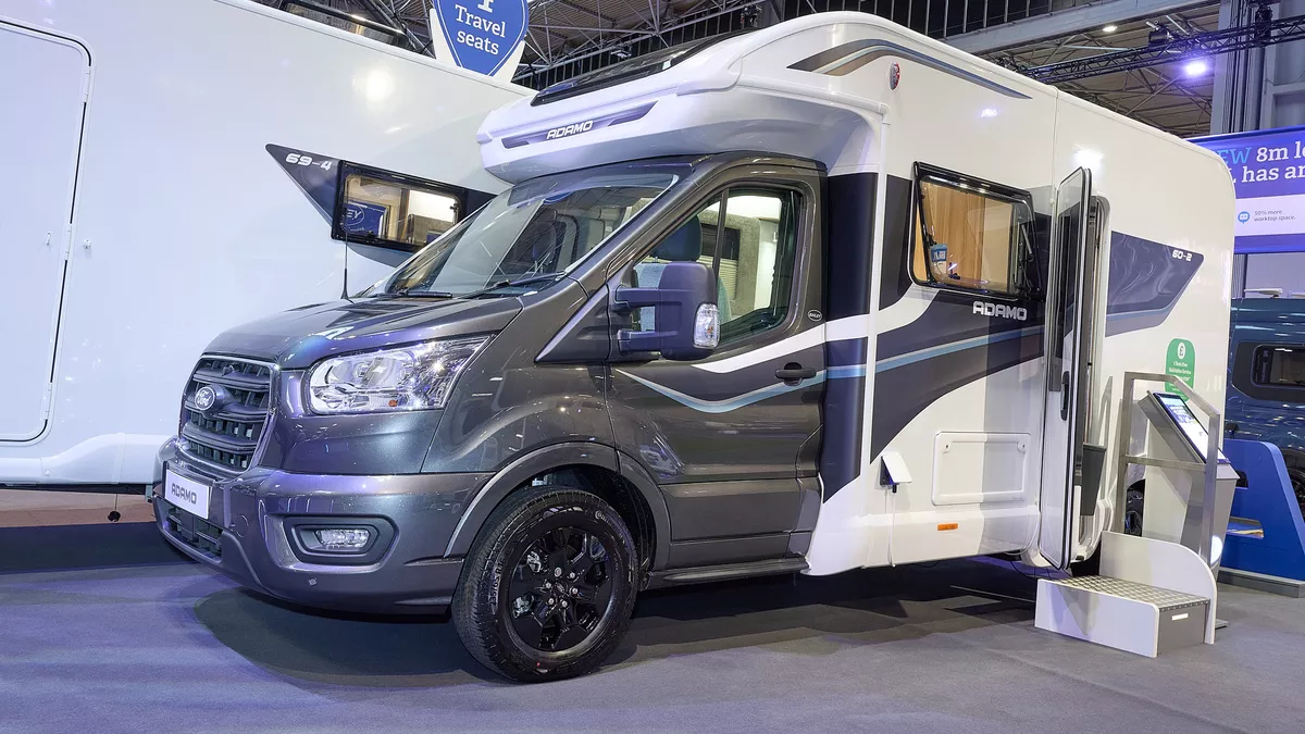 The Bailey Adamo 60-2 has a grey cab with a white body and has grey and blue decals.  There is a white and metal step by the habitation door.  There is an interactive stand to the right of the step. 