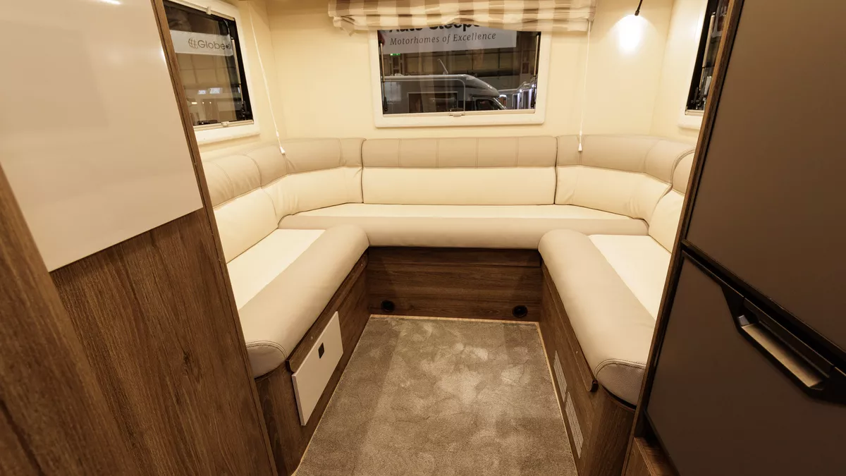 The Roller Team T-Line 700 has a cream/beige u shaped sofa with wooden panelling.  There are three windows with a striped Roman blind at the rear.