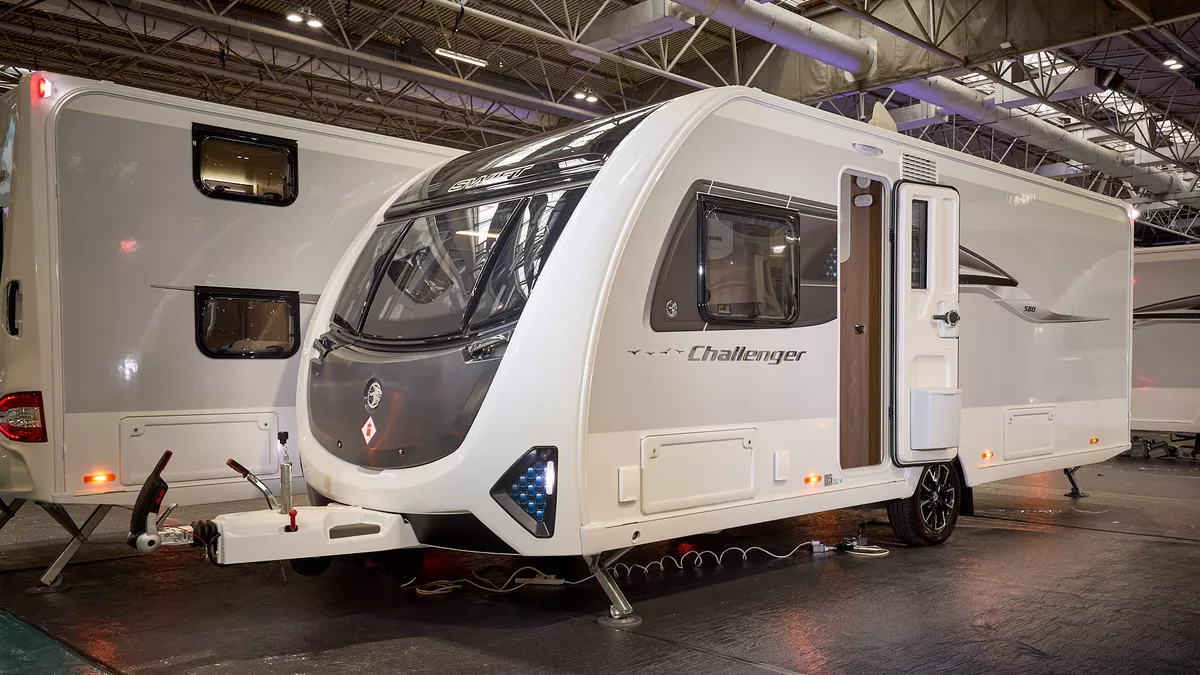 Swift Challenger 580 is white with grey sides and a black front panel.  There are turquoise triangular panels at the front.  Its corner steadies are down and its entrance door is open.