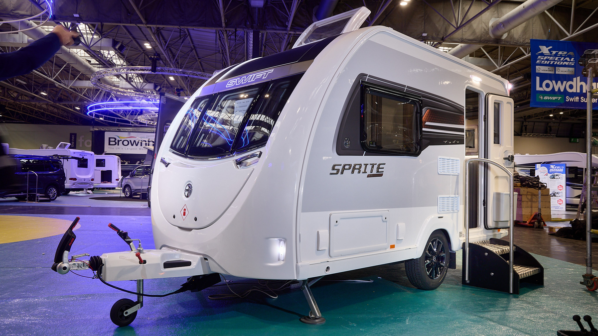 Swift Sprite Exclusive Compact’s exterior is white with grey sides, it has a black and copper decal.  Its entrance door is open with two metal steps to gain easy access.  It has a roof light open.