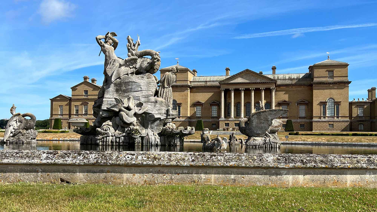 Holkham Hall on a sunny day with a large stone sculpture in front