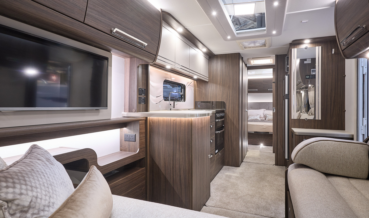 Buccaneer Barracuda interior, it is cream with dark wood furniture.  There is a L shaped sofa at the front.  The fixed bed is beyond the kitchen and there are large skylights.  