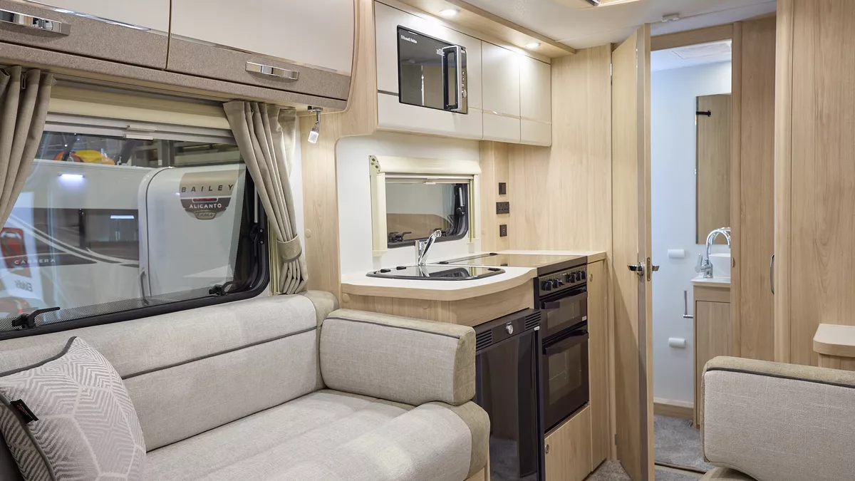 The Elddis Accordo 105 has a beige carpet, with cream and pale brown cabinets.  The upholstery is cream and pale brown with dark brown piping.  Through the opened interior door is a rear washroom.
