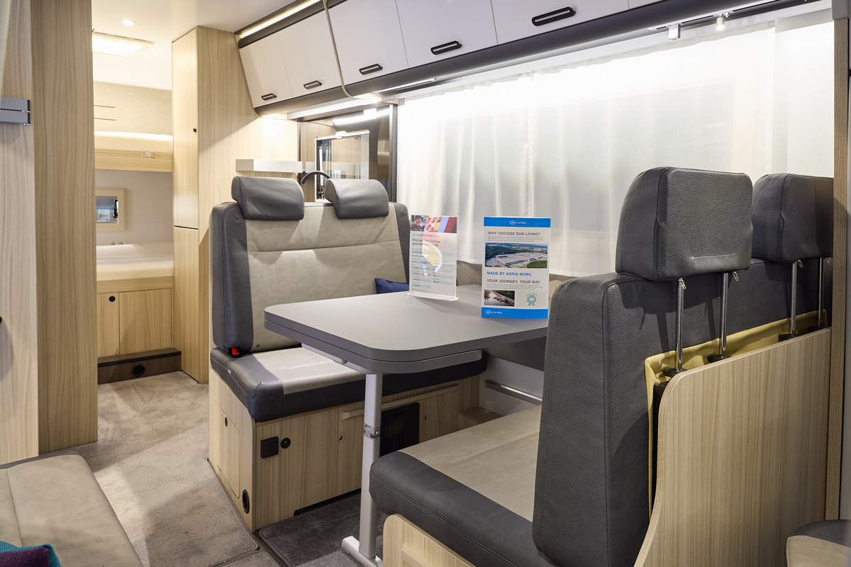 The Sun Living A Series 70DK has beige carpet and its upholstery is dark brown with cream inserts.  The cabinets are white and dark wood.  Towards the rear there are fixed bunks.
