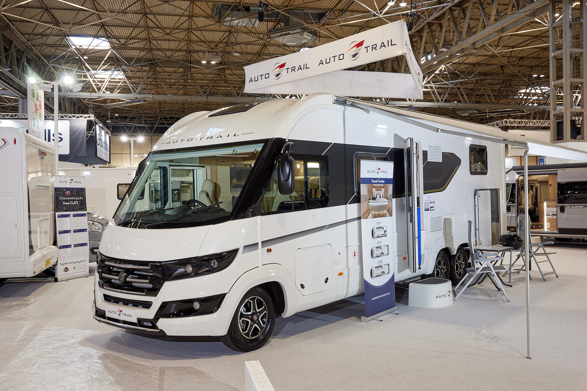 Auto-Trail Grande Frontier GF-88 exterior, the A Class is white, the habitation door is open showing into the interior, with a step to gain easy access.  There is a blue Auto-Trail umbrella in the door.  Its awning is extended with chairs and a table