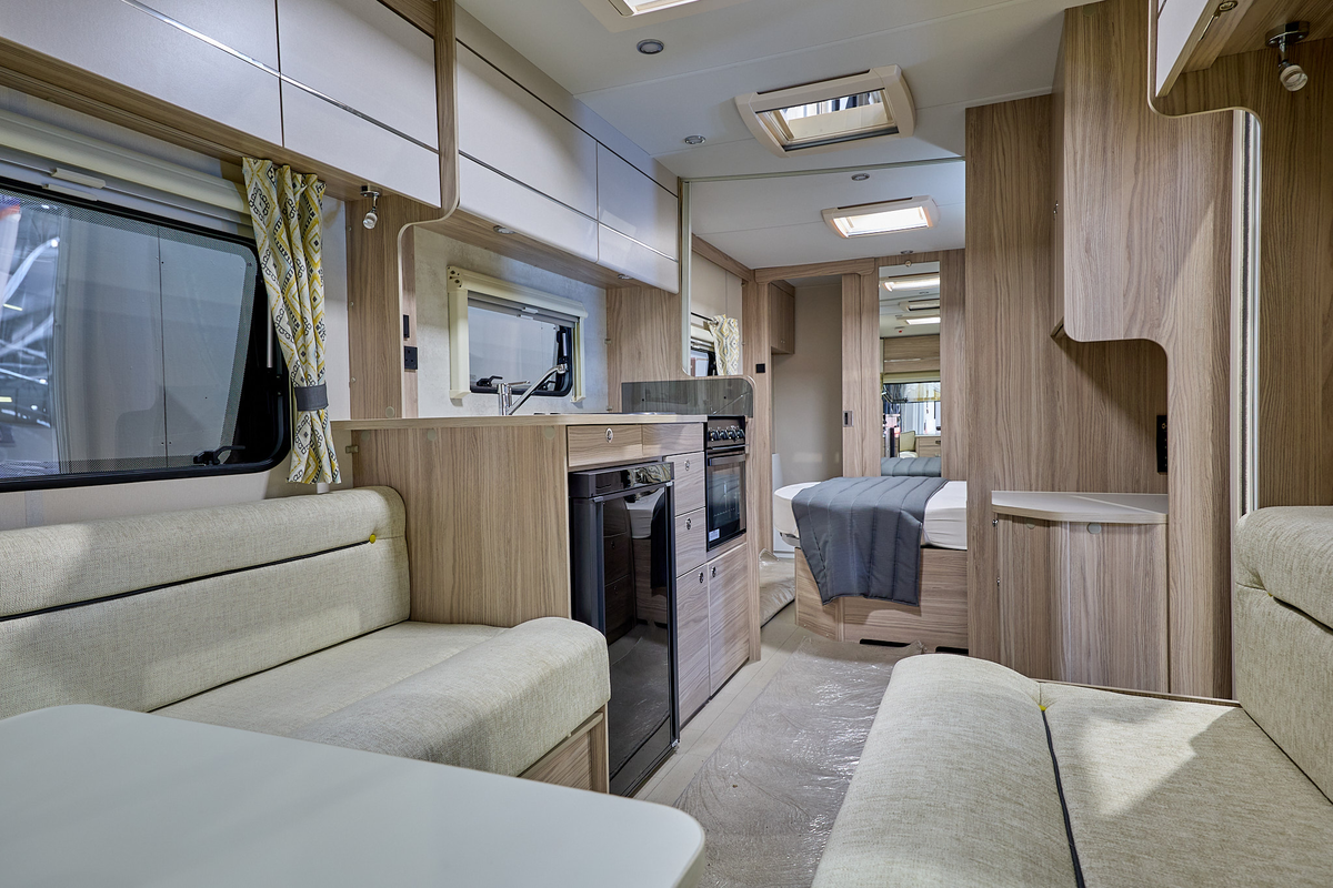 Xplore 554's interior has wooden furniture and has cream sofas with black piping.  There is a central kitchen and the bedroom is just beyond.  The rear washroom's door is open.