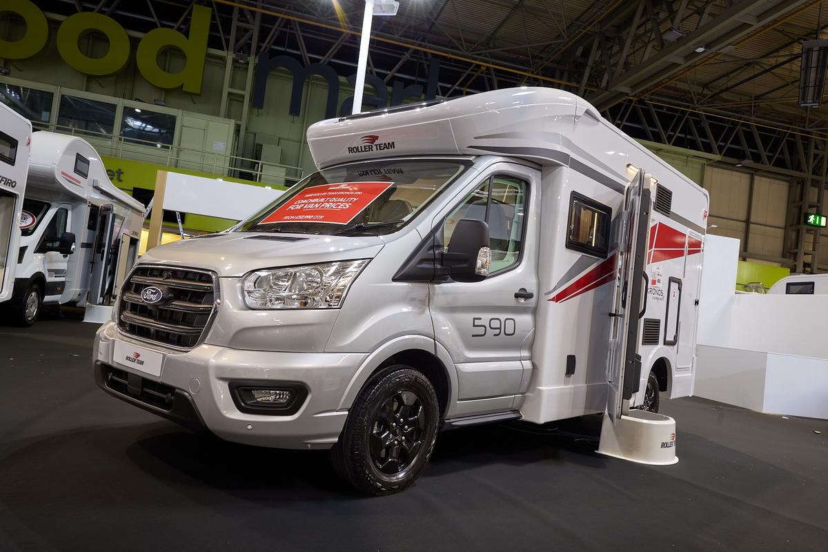 The Roller Team Kronos Compact 590 has a silver cab and white body with grey and red decals.  There is a white step outside the open habitation door. 