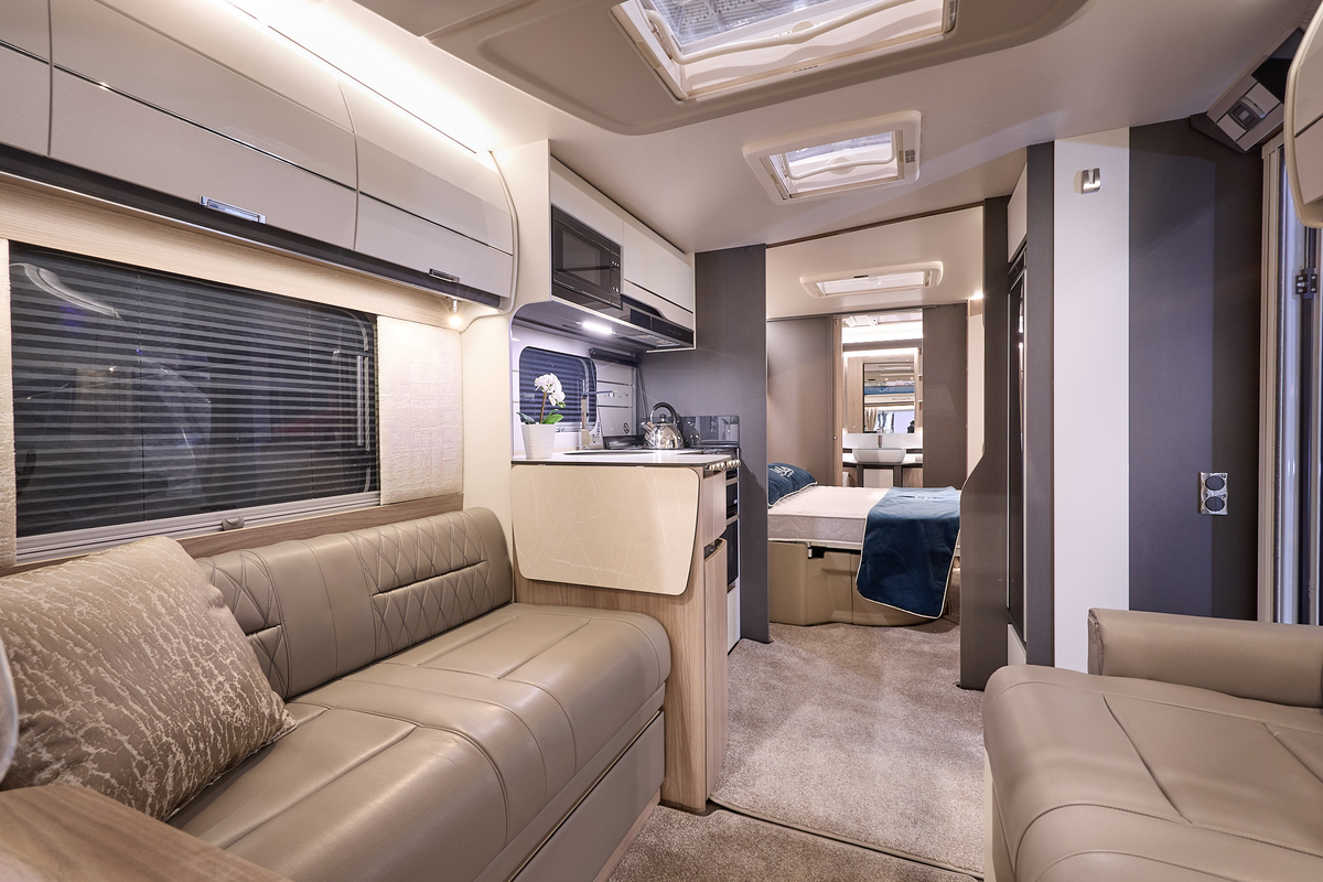 Swift Elegance Grande 780's interior has tan leather upholstery with pale cabinets.  The kitchen is placed in the centre with the bedroom just beyond.  There is a rear washroom and its door is open.