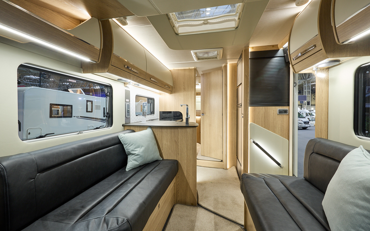 Auto-Trail Grande Frontier GF-80's interior has brown leather upholstery with pale grey cushions.  The furniture is wooden and it has two skylights.  The rear internal door is open revealing the bedroom.