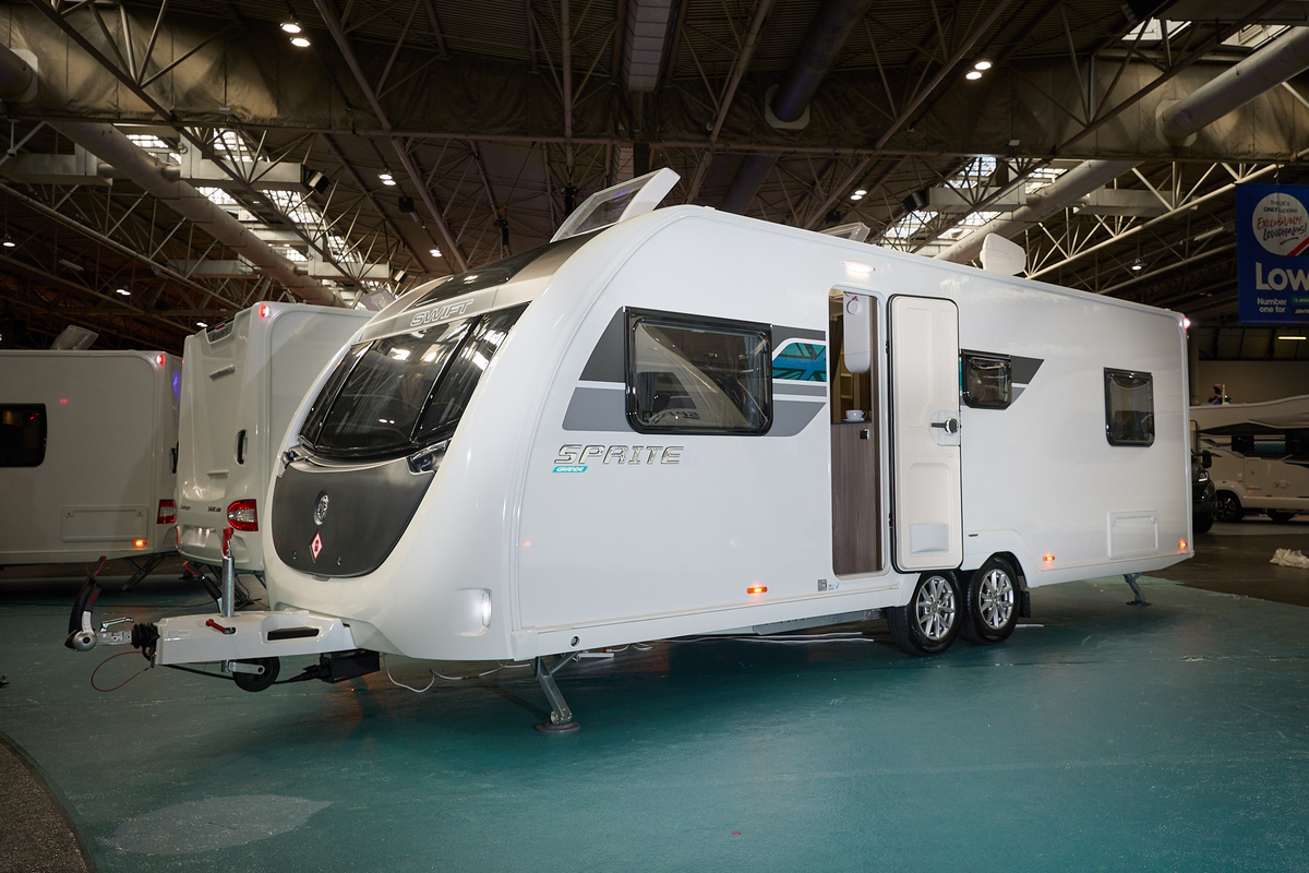 Swift Sprite Grande Quattro FB has a white exterior with grey and turquoise graphics, it has a black panel under the front window and its skylight is open.  It has a twin axle.