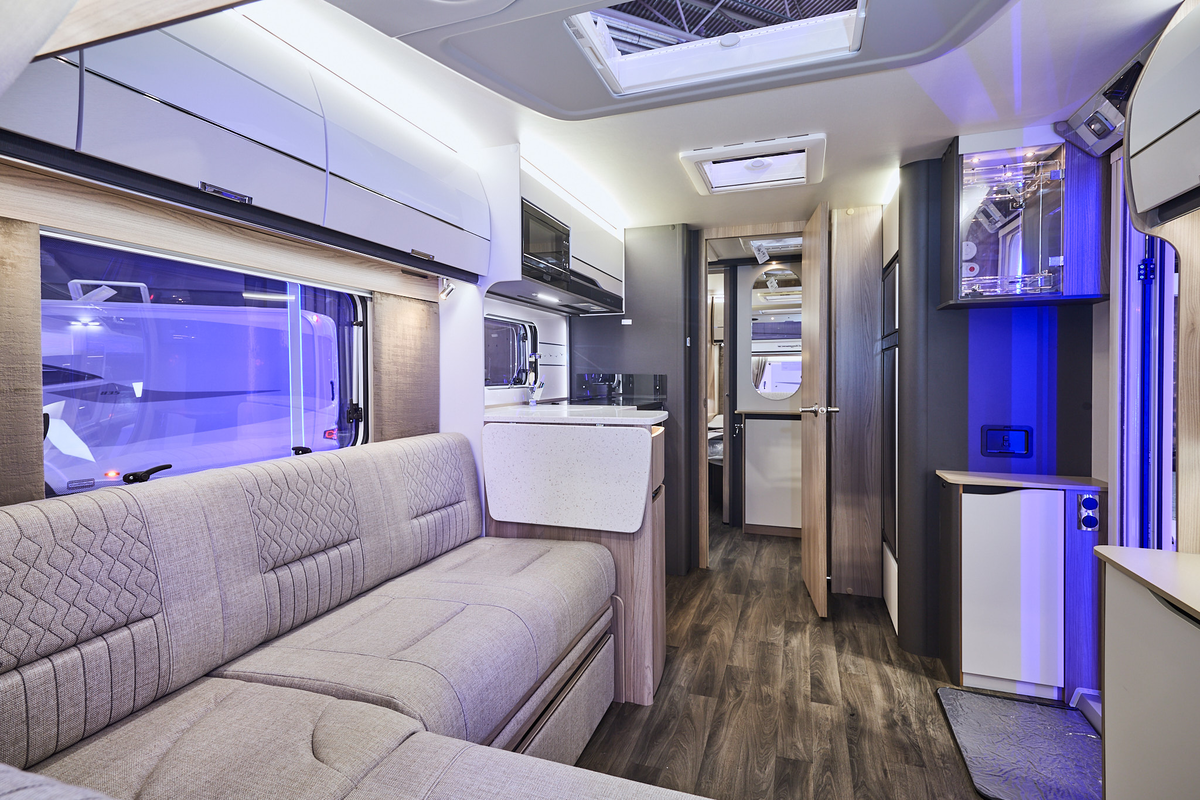Swift Elegance Grande 850L’s interior has wooden units with cream doors.  It has beige upholstery which has embossed patterns.  The internal door is open revealing the washroom and to the rear, the bedroom