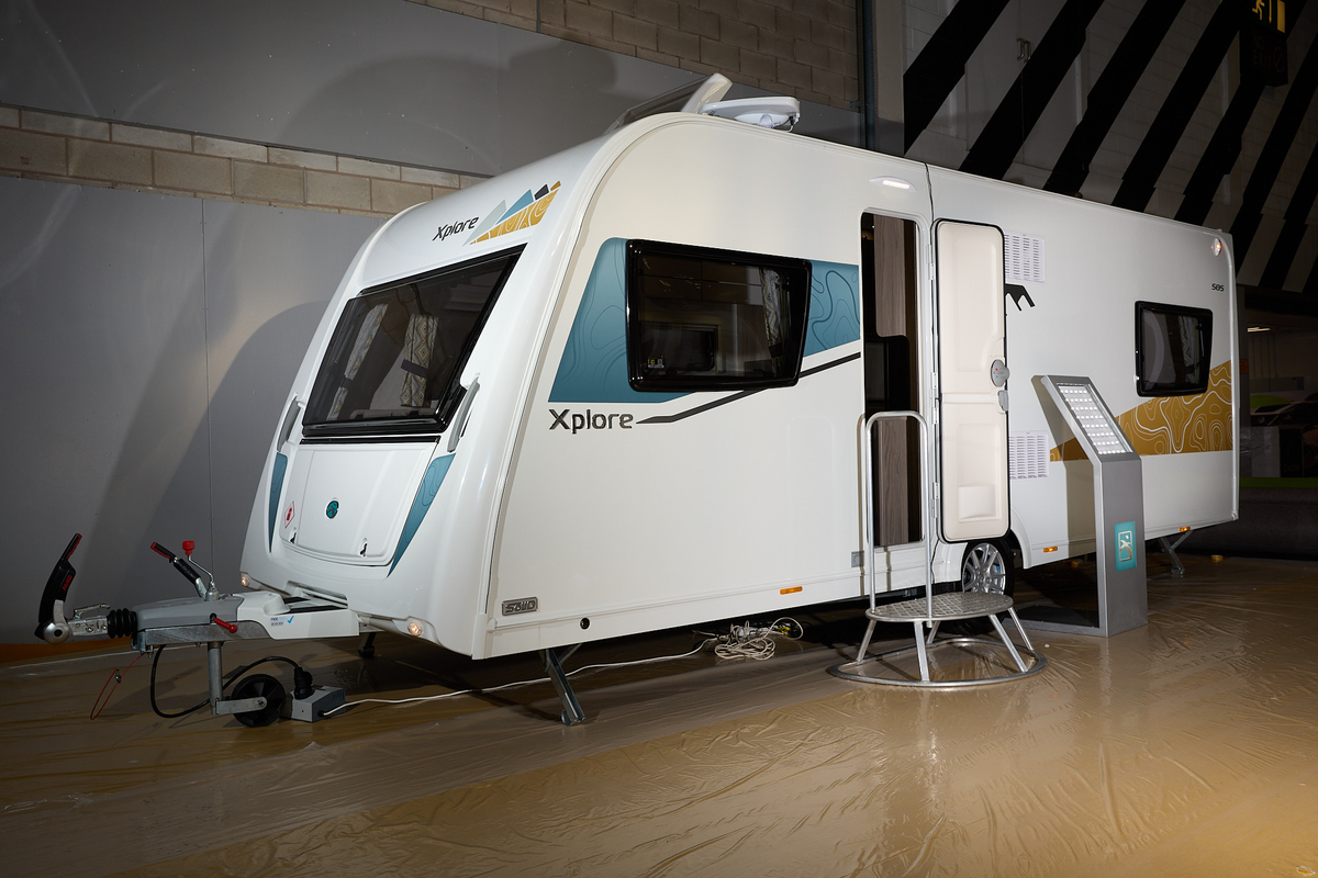 Xplore 585's exterior is white with turquoise and gold graphics, the door is open and there's a metal step for easy access into the interior.