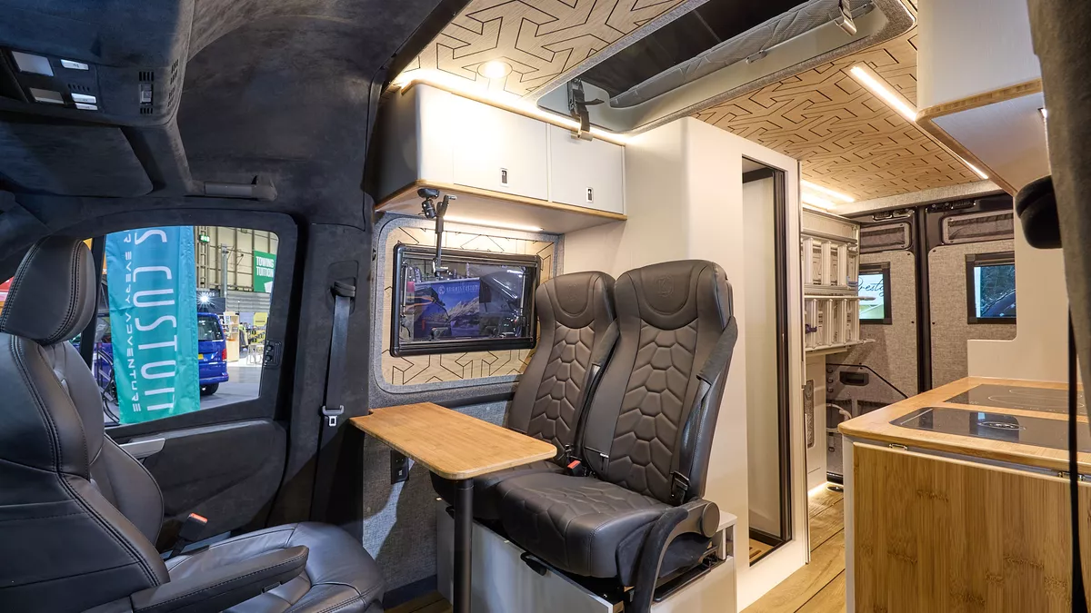 Knights Custom Conversion Prestige XL has wooden flooring with black upholstery.  The cabinets are white and pale wood.  The washroom door is open.  The pop top roof is open.
