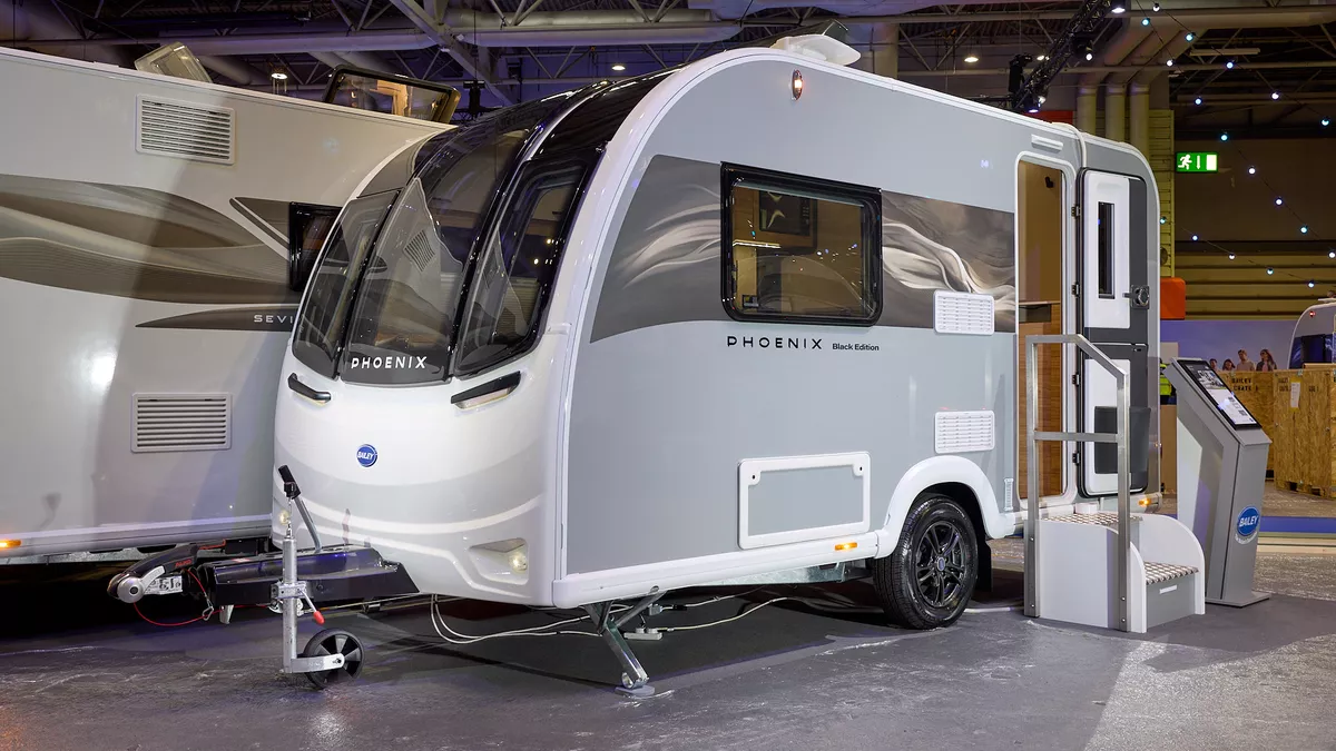 The Bailey Phoenix Black 420 has a grey exterior and a brown decal with light ripples on it.  The entrance door is open and there are two metal steps to gain easy access to the interior.  Next to the steps is an interactive stand.