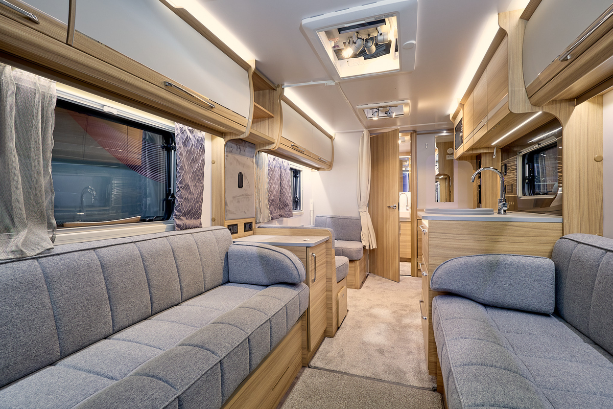 Bailey Unicorn Madrid interior, it is grey with light wood.  There is a dinette beyond the kitchen.  The rear washroom has a wooden door which is open.  There are two skylights.