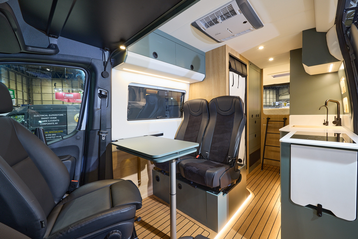 Project Yonder Freedom 4X Utility has a wooden floor with blue cabinets.  The upholstery is black and there is feature lighting under the chairs.  There is a ladder to the fixed rear bed. 