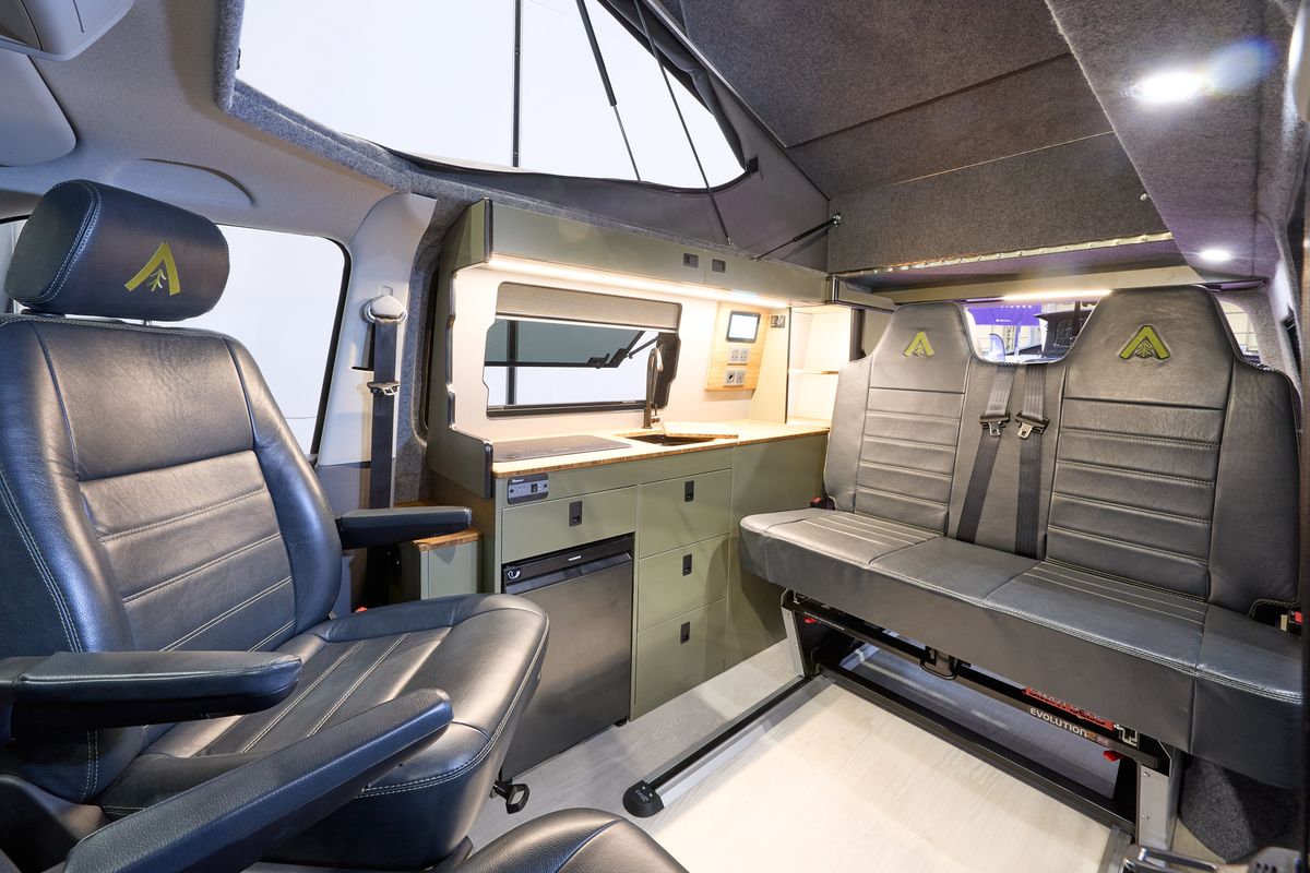 Wildtracks Campervans Explorer has a cream floor with black leather upholstery.  The cabinets are green.  The rising roof is open.