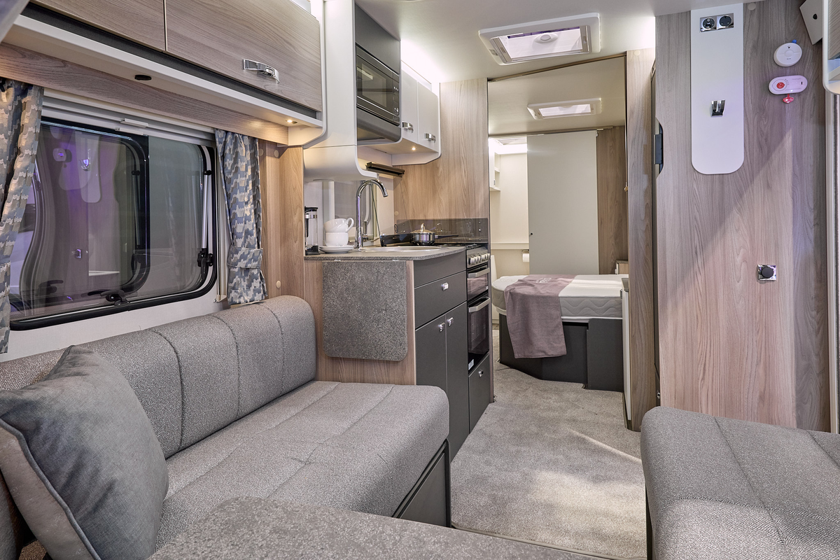 Swift Sprite Major 4 SB’s interior has grey upholstery with wooden furniture.  The kitchen is in the middle and its furniture has dark doors. The fixed bed is beyond the kitchen with a washroom at the end