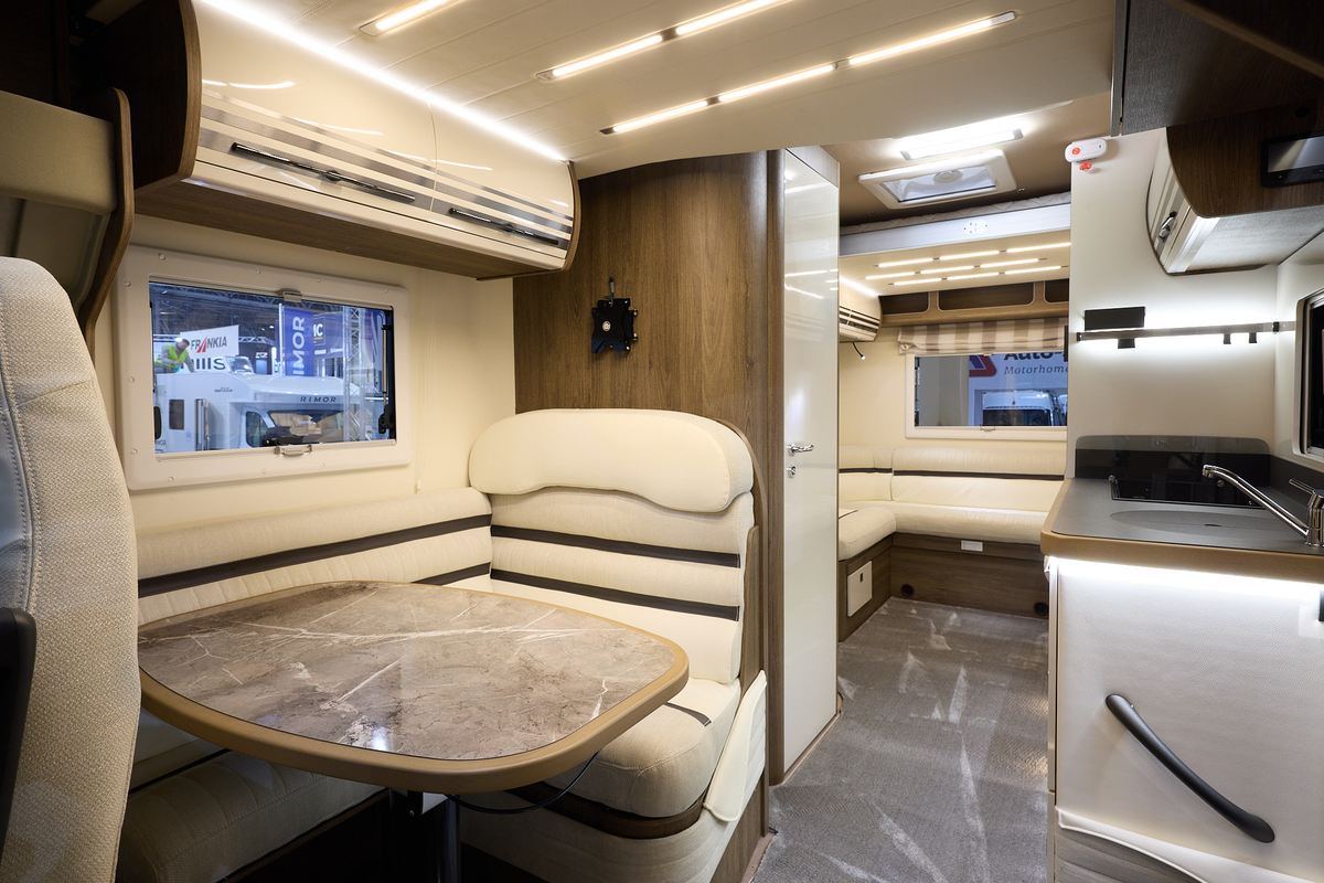 The Roller Team T Line 700 has grey carpet.  The upholstery is cream with dark brown highlights.  There is a marble effect table in front of the sofas.  The cabinets are cream with wooden surrounds.  There is a rear lounge.
