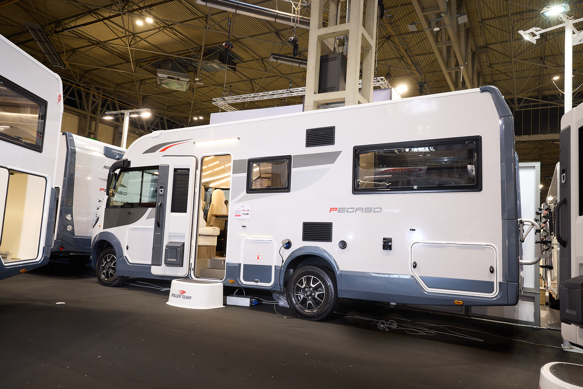 The Roller Team Pegaso 745 is white with blue trim and grey and red decals.  There is a white step outside the open habitation door. 