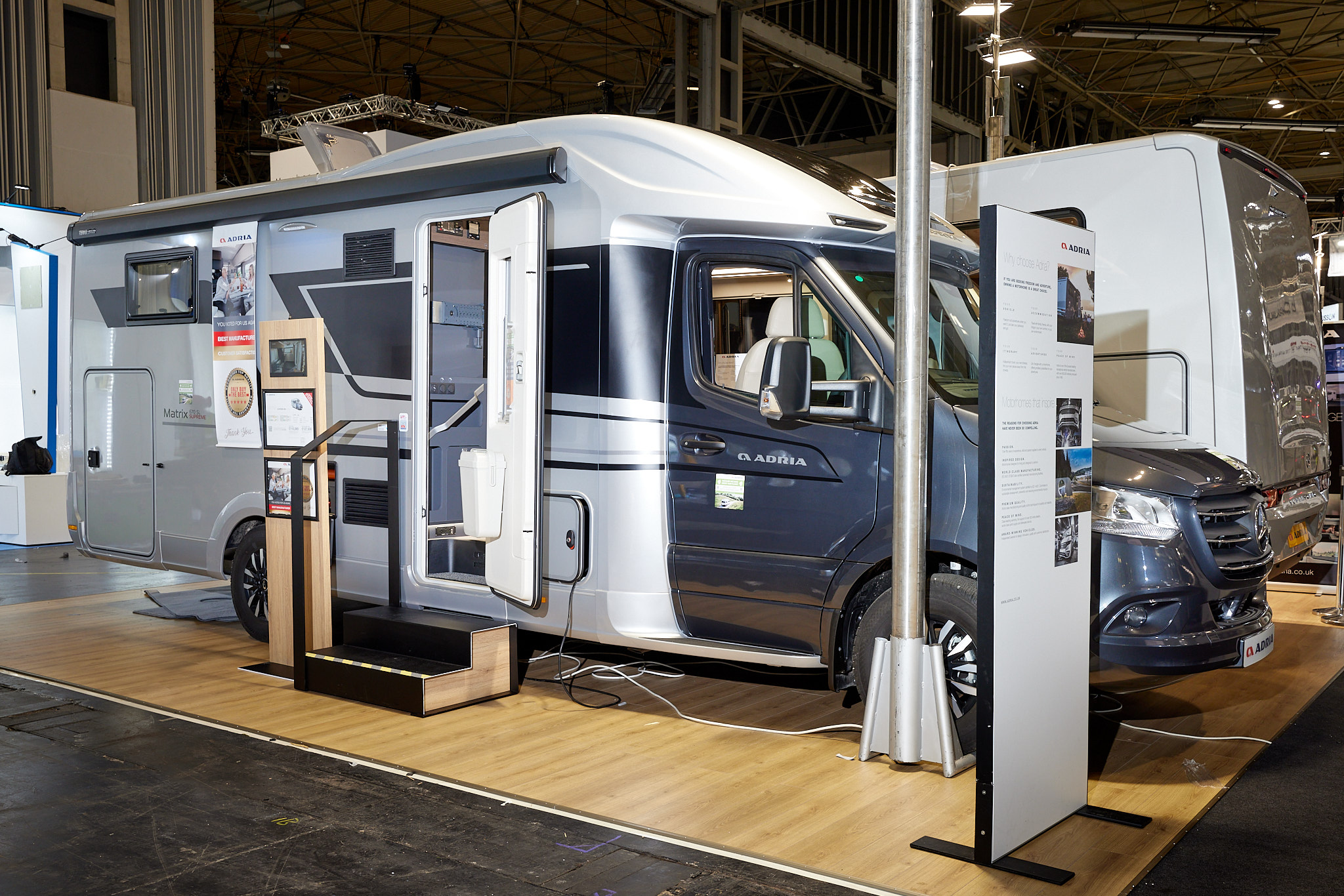 Adria Matrix Supreme MB 670 SL exterior, the motorhome is white with a grey cab, the habitation door is open showing into the interior, with a double step to gain easy access.  The roof light is fully open.