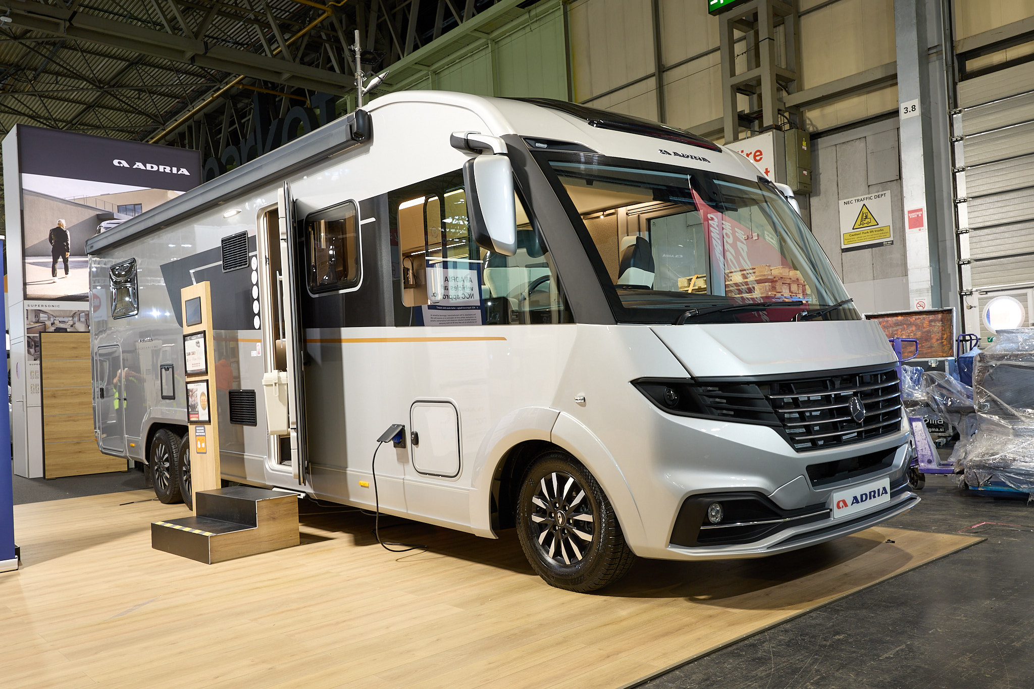 Adria Supersonic’s exterior is silver and black, the entrance door is open and there are wooden steps to gain easy access.  There is an interactive information board by the side of the van.